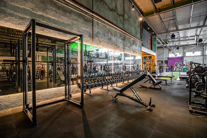 Spacious gym area with a variety of workout machines, weights, and benches, reflecting a modern industrial design.