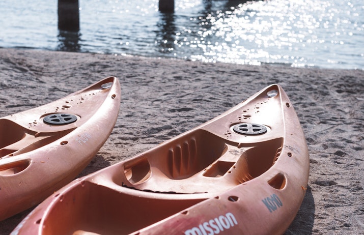 Try Something New Two orange kayaks on a sandy beach beside calm water.
