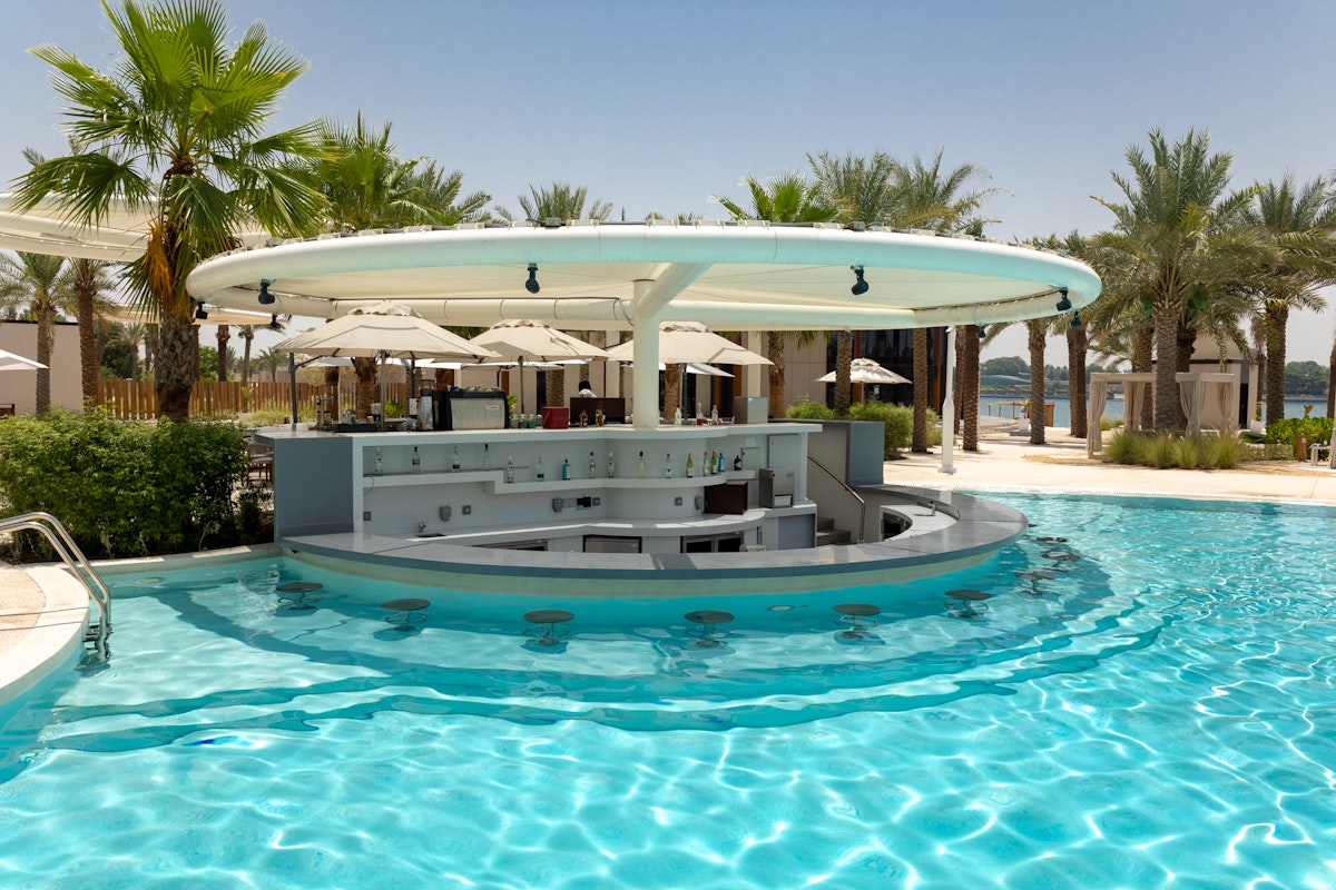Poolside bar with stools and umbrellas, surrounded by palm trees