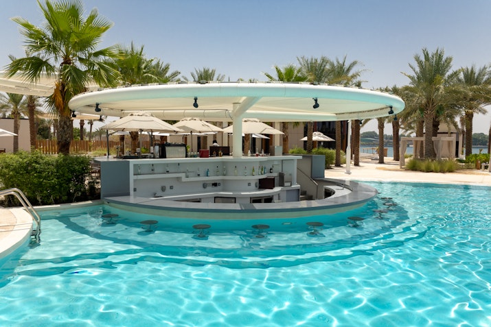Poolside bar with stools and umbrellas, surrounded by palm trees