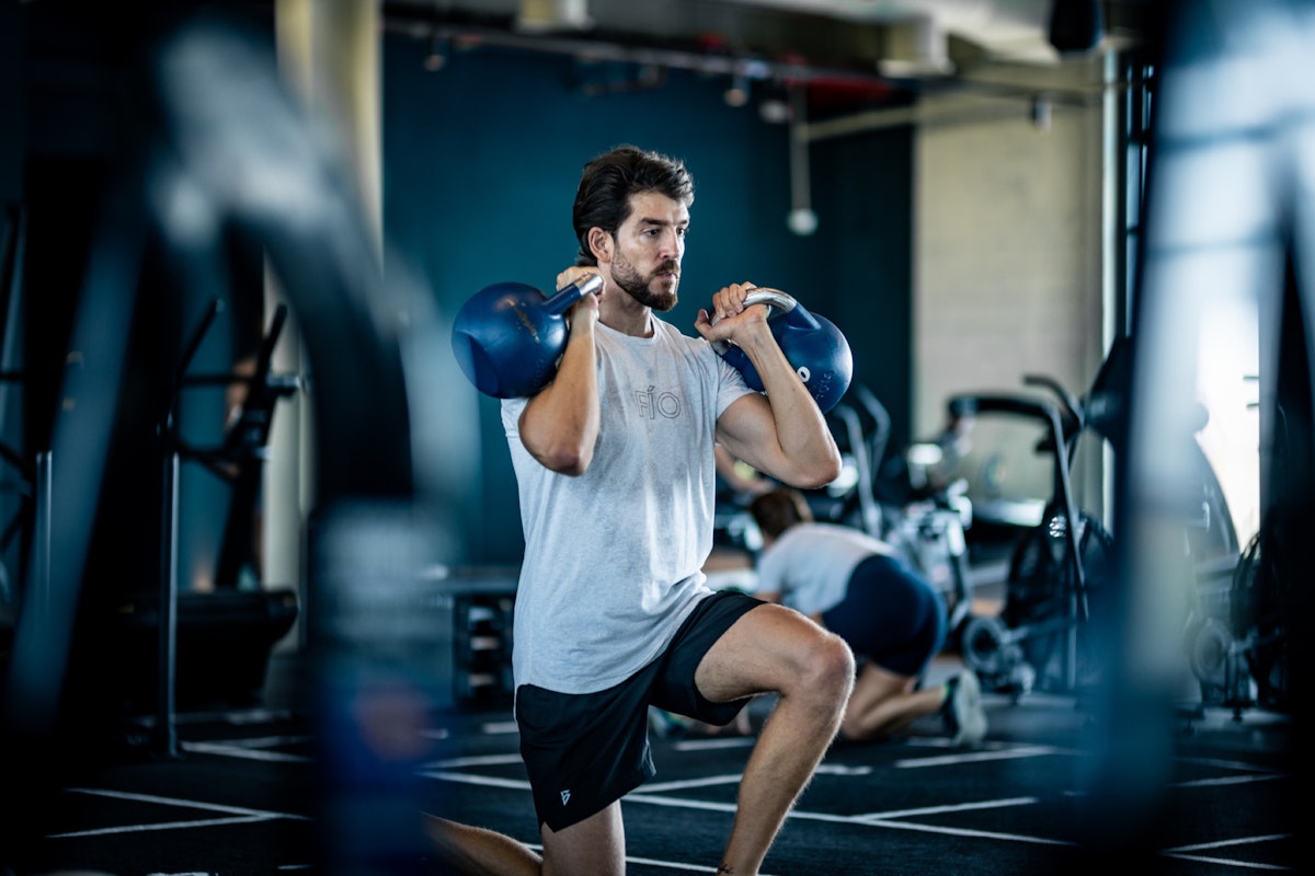 A man performing a lunge exercise with a kettlebell in a gym.