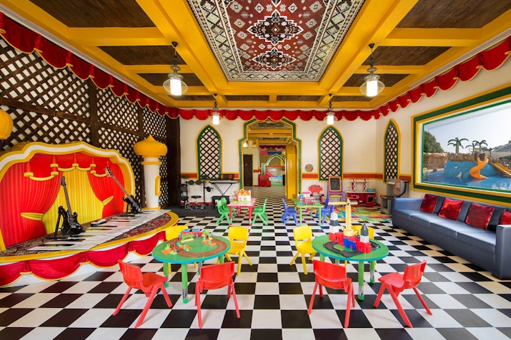 A colorful kids' playroom with checkered floors, vibrant furniture, and a stage-like area with toys and art decorations.