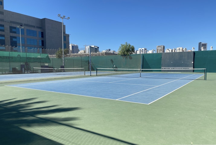 Tennis court with a clear blue sky and city buildings in the background.