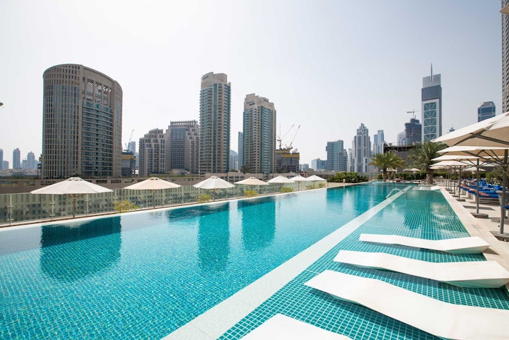 A rooftop infinity pool with city skyscrapers in the background and lounge chairs by the poolside.