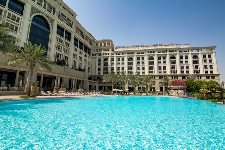 Hotel pool with clear water, surrounded by palm trees and a large building in the background.