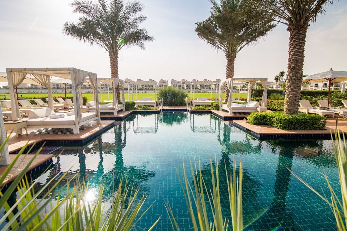 Poolside cabanas surrounded by lush greenery and palm trees, with a serene view of the resort in the background.