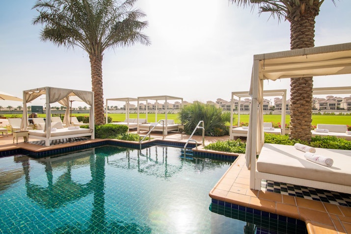 Poolside cabanas surrounded by lush greenery and palm trees, with a serene view of the resort in the background.