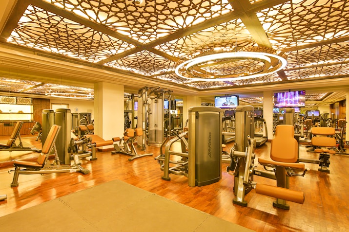 A well-lit gym with exercise machines and decorative ceiling lights.