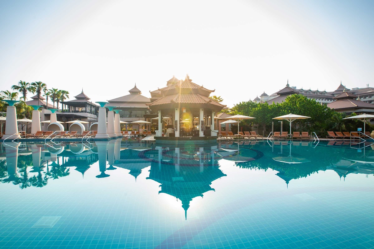 Anantara The Palm Dubai Resort A serene pool with reflections of a pagoda-like structure and surrounding lounge chairs, bathed in sunlight.