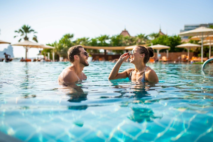 A couple enjoying a playful moment in a swimming pool on a sunny day.