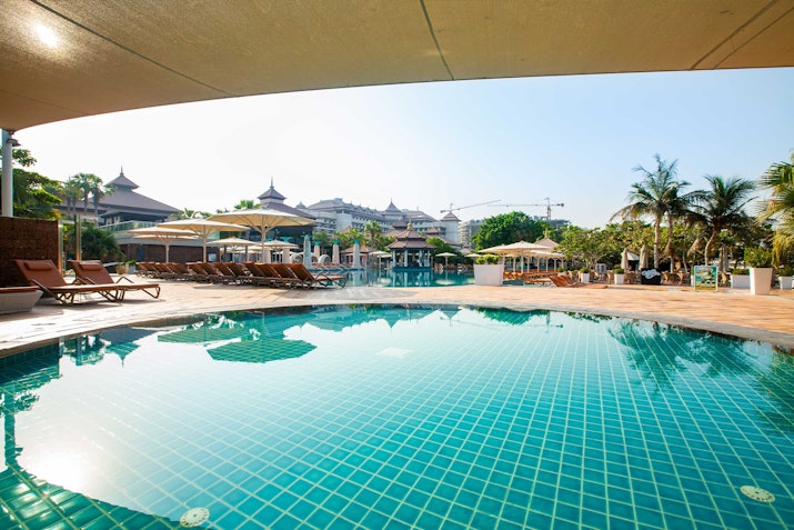 View of a clear swimming pool surrounded by lounge chairs and palm trees.