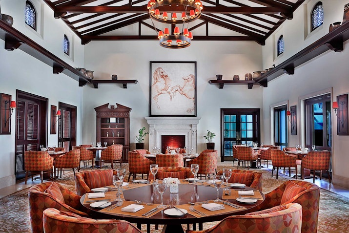 A spacious and elegant dining room with a round table set for a meal, surrounded by cozy chairs and a large chandelier.