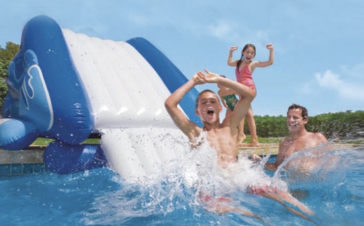Children and an adult enjoying a water slide at the pool.