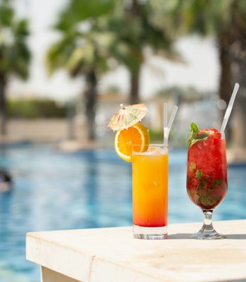 Fairmont Bab Al Bahr Two refreshing cocktails with fruit garnishes placed by the poolside.