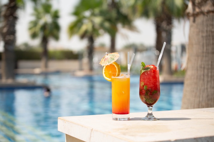 Two refreshing cocktails with fruit garnishes placed by the poolside.
