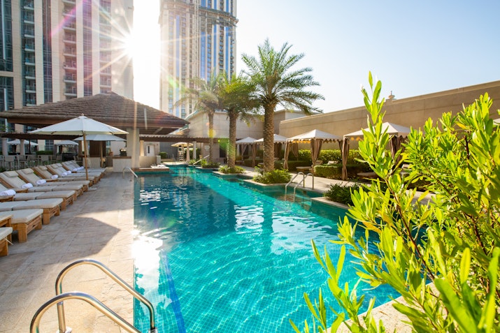 A poolside scene with loungers and palm trees, sunlight reflecting off the water.