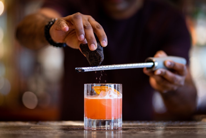 Bartender garnishing a cocktail with grated ingredients