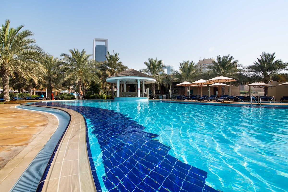 InterContinental Abu Dhabi A swimming pool with a curved edge, featuring blue tiles and surrounded by palm trees and sun loungers.