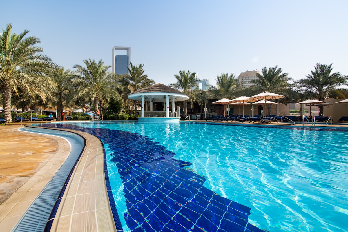 A swimming pool with a curved edge, featuring blue tiles and surrounded by palm trees and sun loungers.