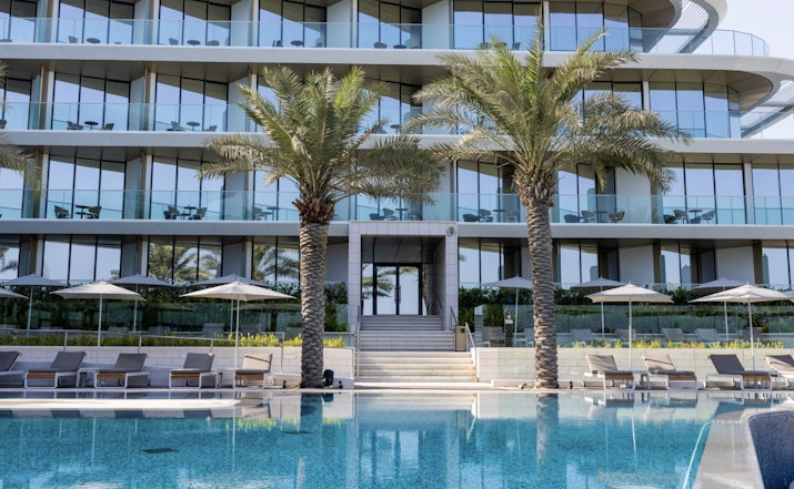Luxury poolside with palm trees and glass building backdrop.