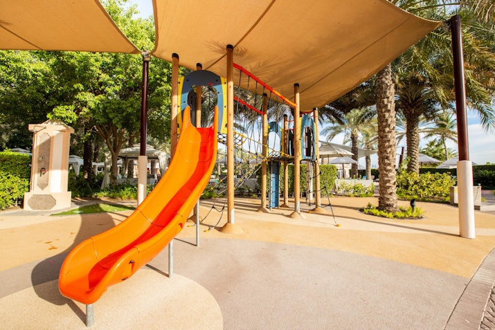 Orange slide in a playground with palm trees in the background.