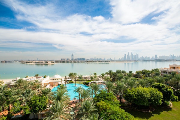 Panoramic view of a resort with a pool and lush gardens, overlooking the skyline and waterfront