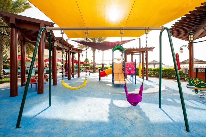 Playground with swings and colorful seating, shaded by a yellow canopy.