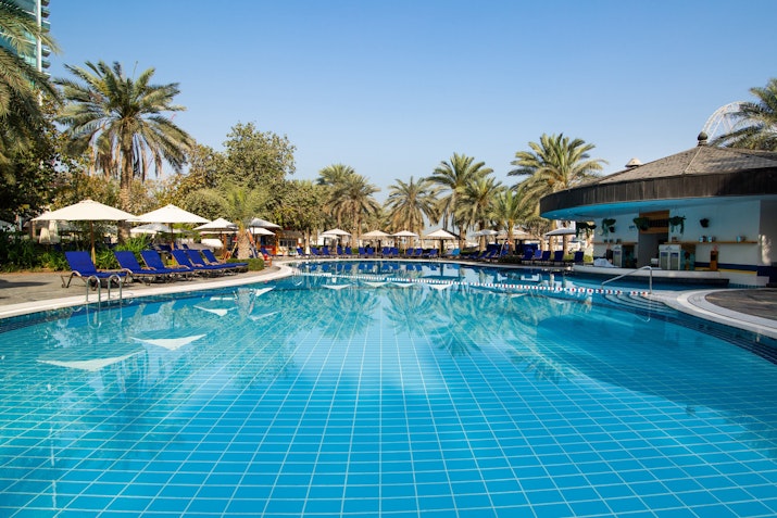 Swimming pool with blue tiles and lounge chairs under umbrellas.