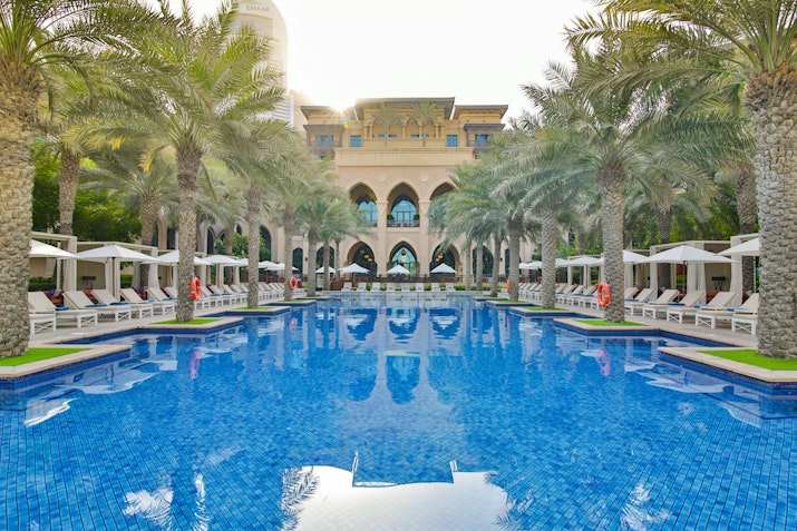 Luxury hotel pool with palm trees and lounge chairs, reflecting the architecture in the water