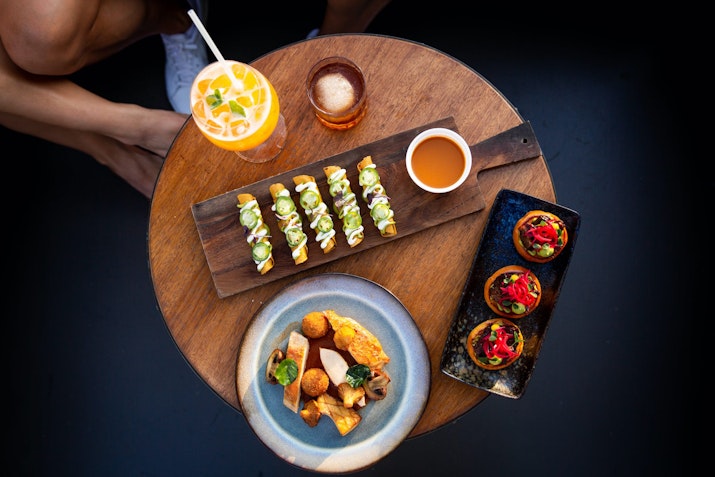A table with sushi, cocktails, and appetizers served on plates.