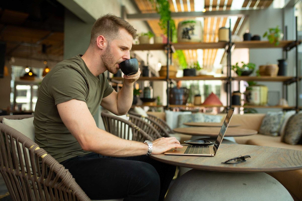 Man working on a laptop in a stylish, cozy setting with a cup of coffee.