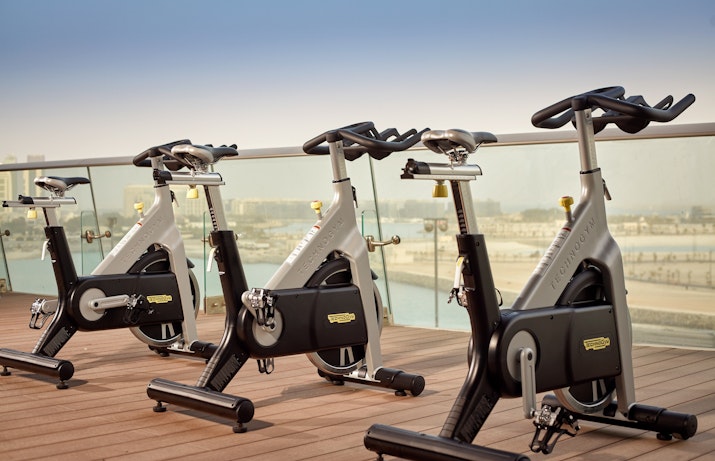 A line of stationary bikes on an outdoor terrace overlooking a scenic view with blue skies