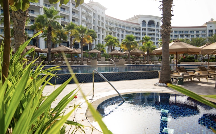 Resort pool area with tropical greenery and sun loungers.