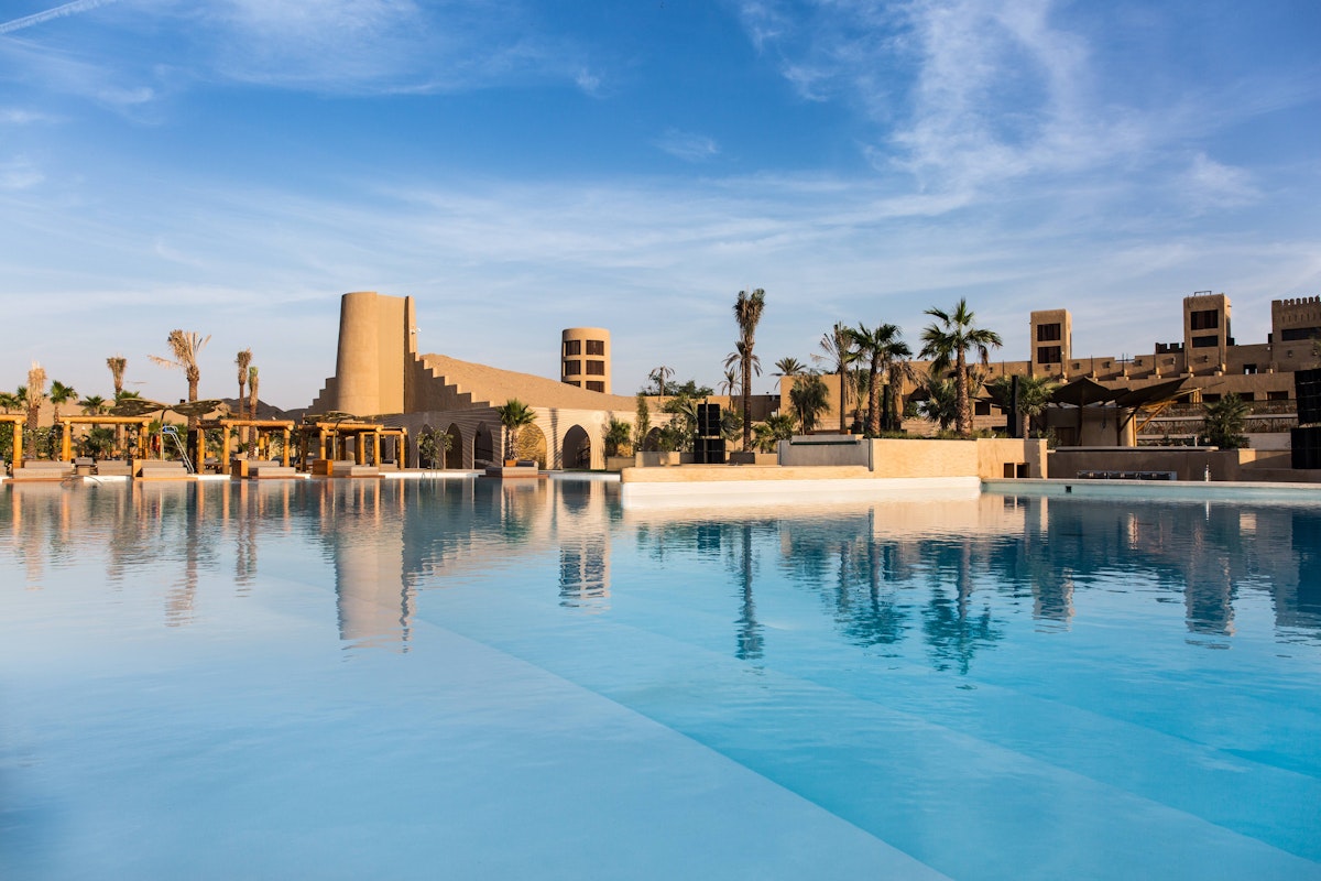 A serene pool reflecting the sky, surrounded by desert-inspired architecture and palm trees.