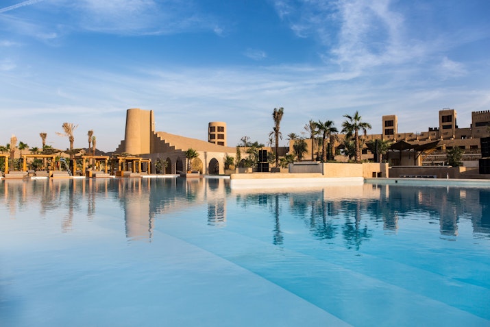 A serene pool reflecting the sky, surrounded by desert-inspired architecture and palm trees.