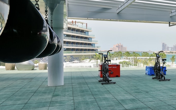 A fitness area with workout equipment outdoors, with a view of a building and palm trees in the background.