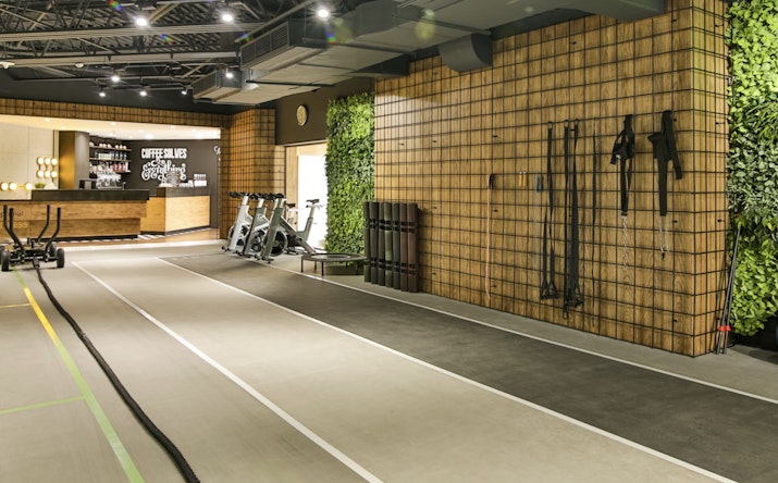 A fitness room with a modern design, featuring exercise equipment, a green wall, and a coffee bar in the background.