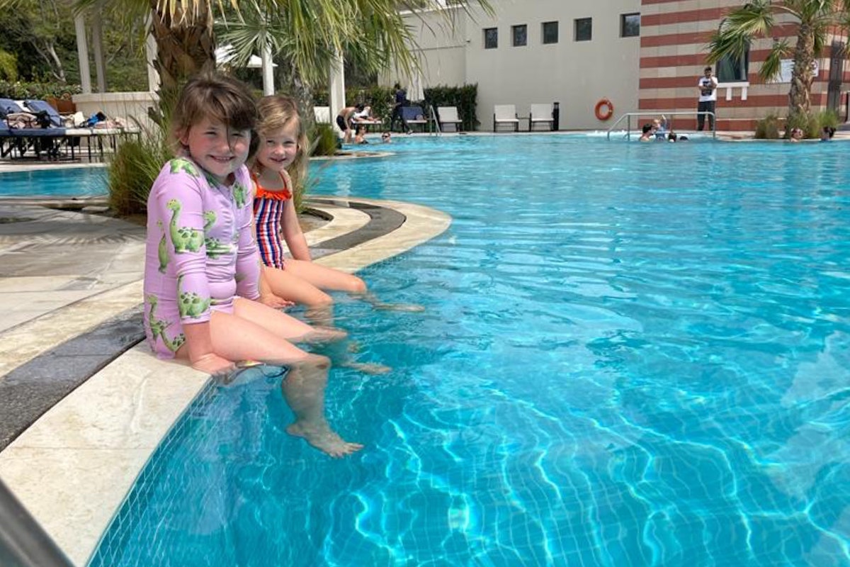 Two girls sitting at the edge of a pool, dipping their feet in the water.