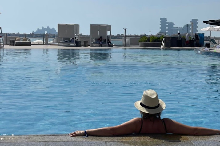 Taj Exotica Resort and Spa A person in a hat relaxing by the edge of a pool, with a clear view of the horizon.