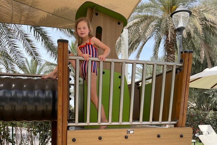 The Els Country Club A girl standing on a playground structure, wearing a red and white striped swimsuit.