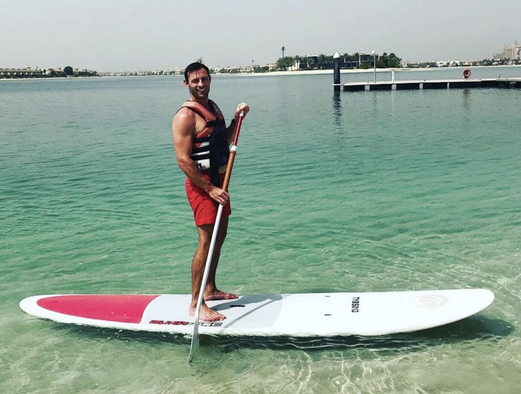 A man in a life jacket standing on a paddleboard in clear water.