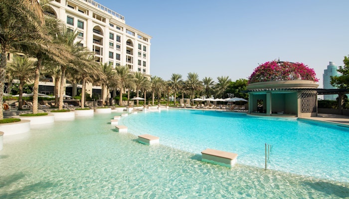 Palazzo Versace Dubai A luxurious pool with clear water, surrounded by palm trees and a hotel building in the background.