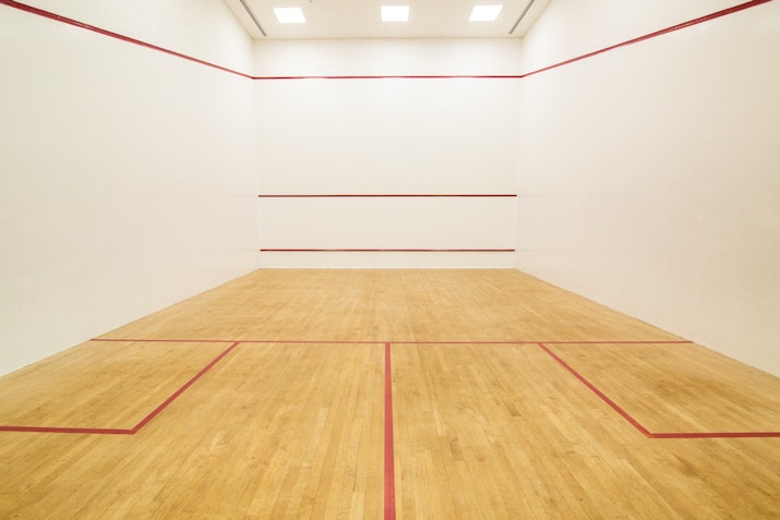 An empty squash court with wooden flooring and red boundary lines.