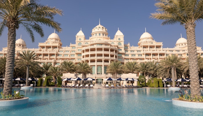 Raffles The Palm Dubai Grand hotel with ornate architecture featuring domed roofs, situated beside a large swimming pool surrounded by palm trees