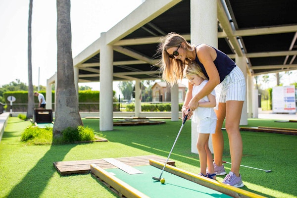 A mother and her child playing mini-golf outdoors on a sunny day.