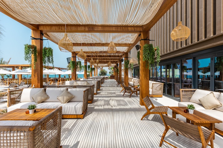 Outdoor lounge with wooden pergola, wicker furniture, and hanging plants.