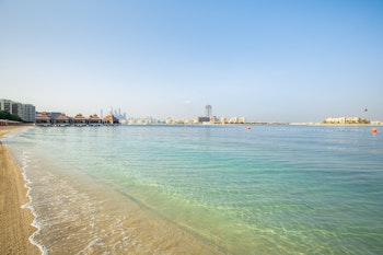 A peaceful beach with clear water, surrounded by resorts and distant city skyline.