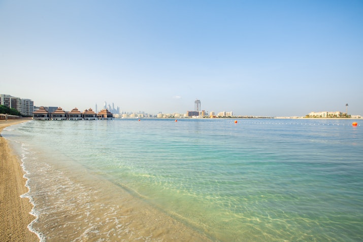 A peaceful beach with clear water, surrounded by resorts and distant city skyline.