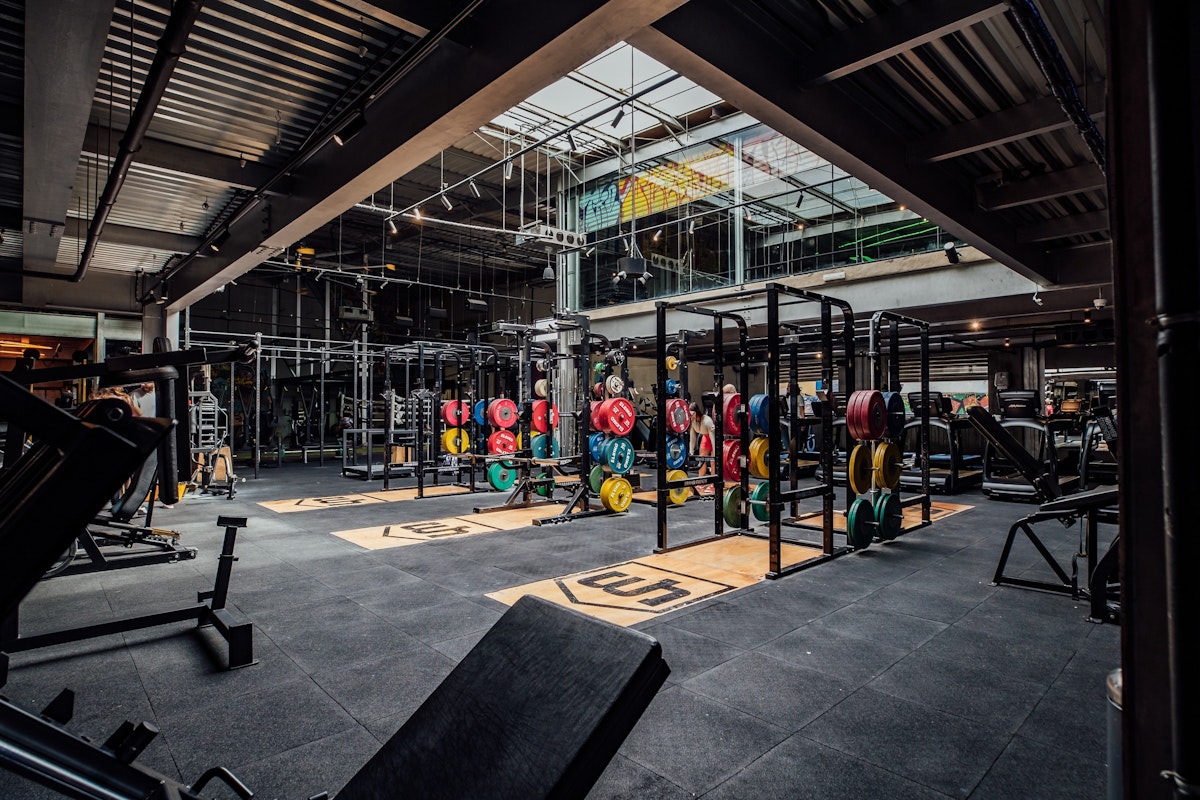 Interior of a gym with workout equipment, weightlifting bars, and colorful weights.