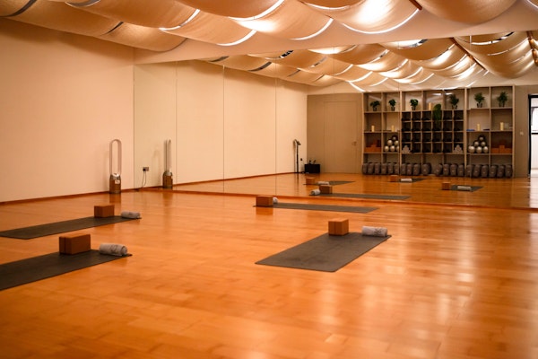 A calming yoga studio featuring neatly arranged mats, blocks, and towels on a polished wooden floor, with soft ceiling drapes and warm lighting creating a peaceful ambiance.